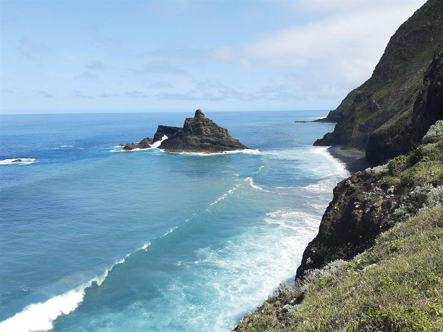 Rocky sea stack and rugged green cliffs along the coast at Boaventura, Madeira, with waves breaking below