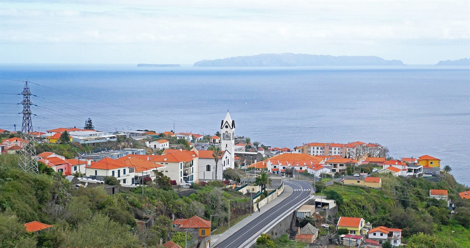 Caniço on Madeira's south-east coast: red-roofed houses and the parish church on the slope above the Atlantic, with the coast road below