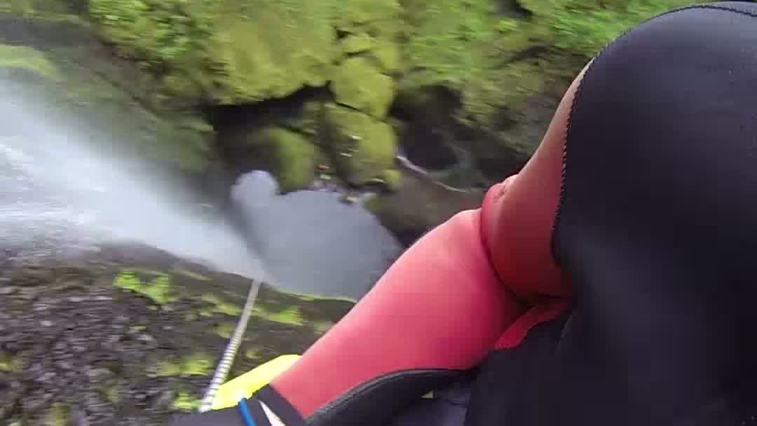 Canyoner in een wetsuit en tuig die langs een waterval abseilt aan een touw bij Ribeira da Hortelã, Madeira