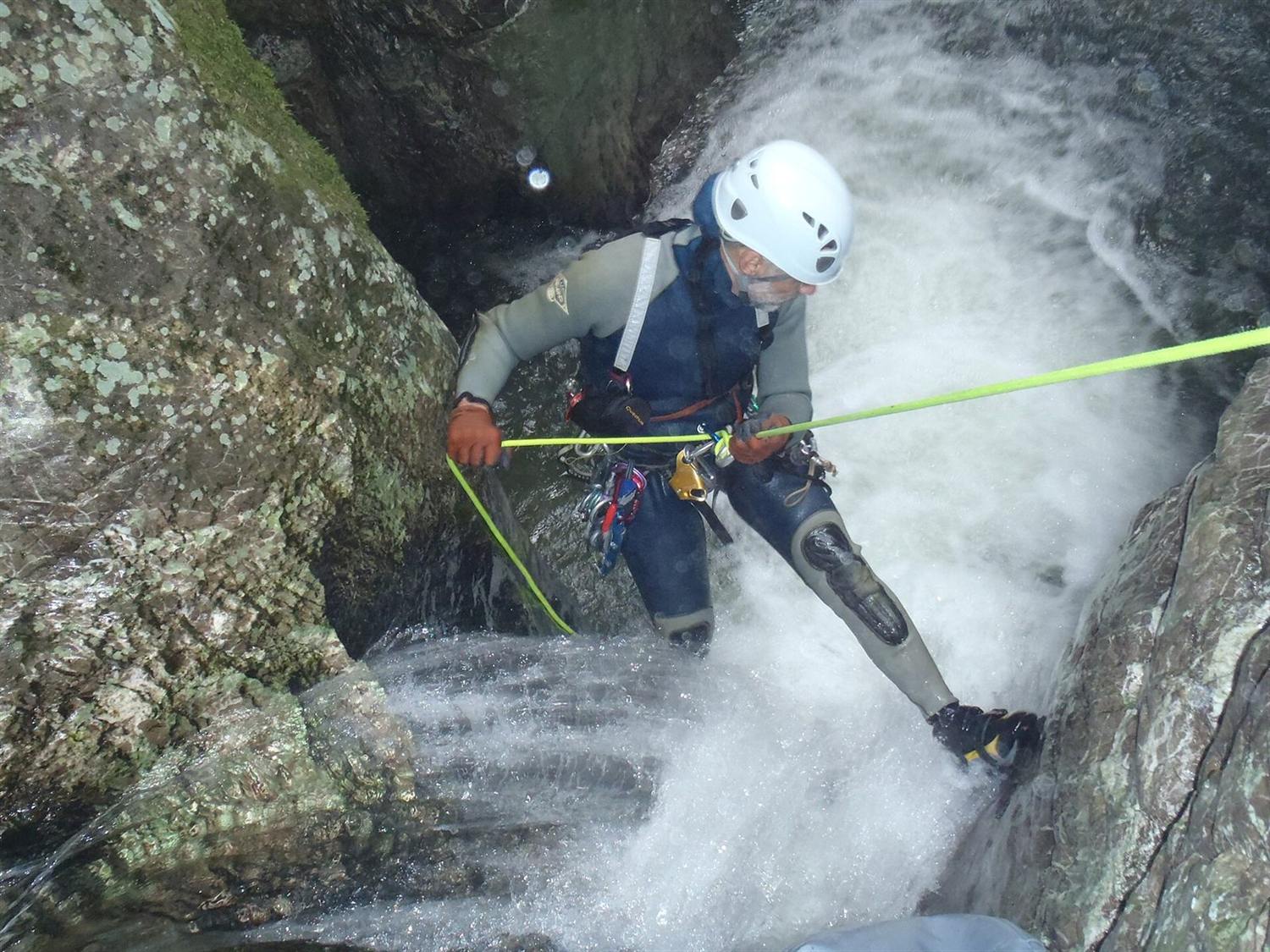 Canyoner in wetsuit and helmet rappelling down a rushing waterfall on a green rope