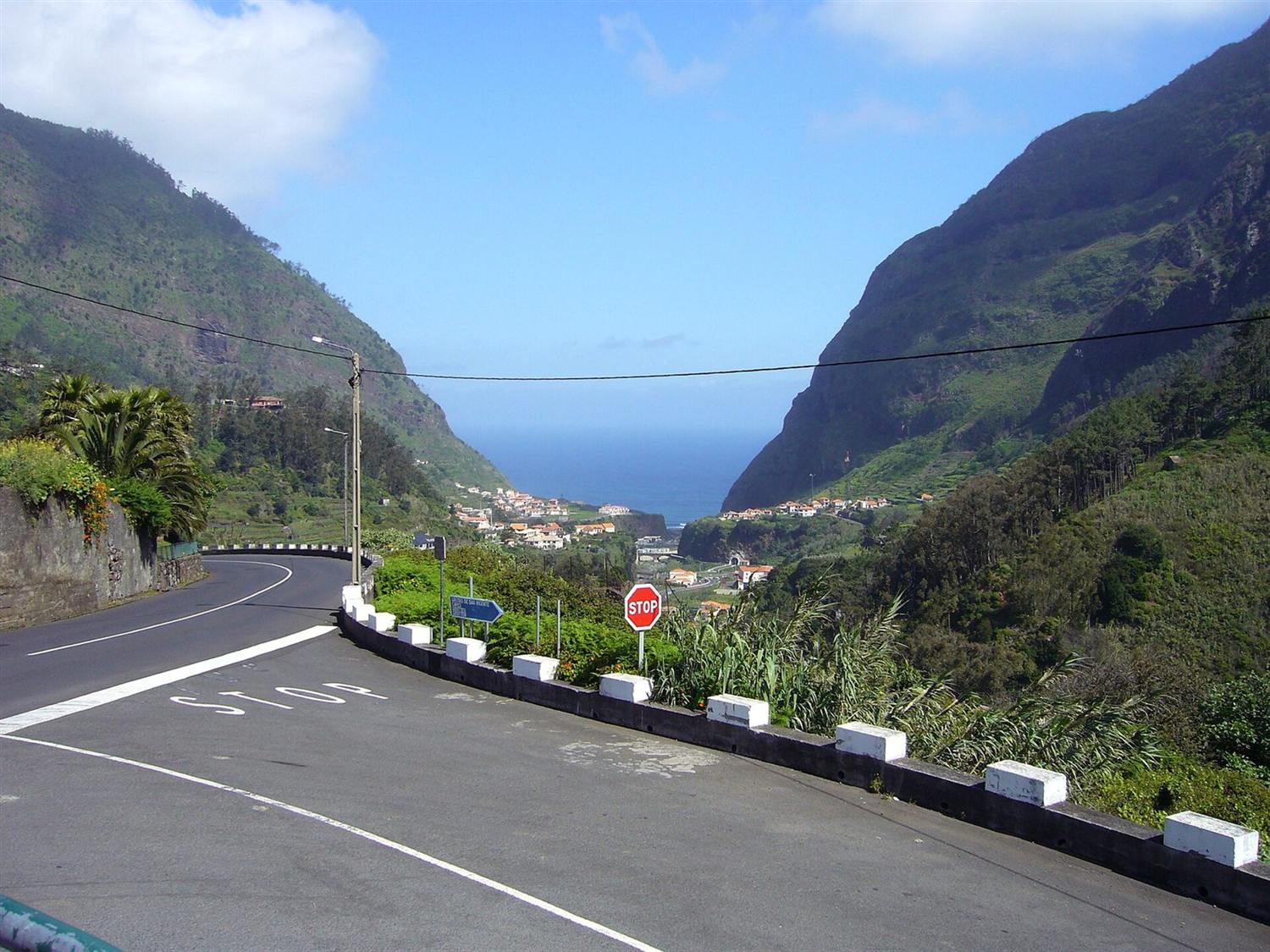 Kurvenreiche Bergstraße mit Stoppschild, die hinab ins Tal von São Vicente und zur Atlantikküste führt, Madeira
