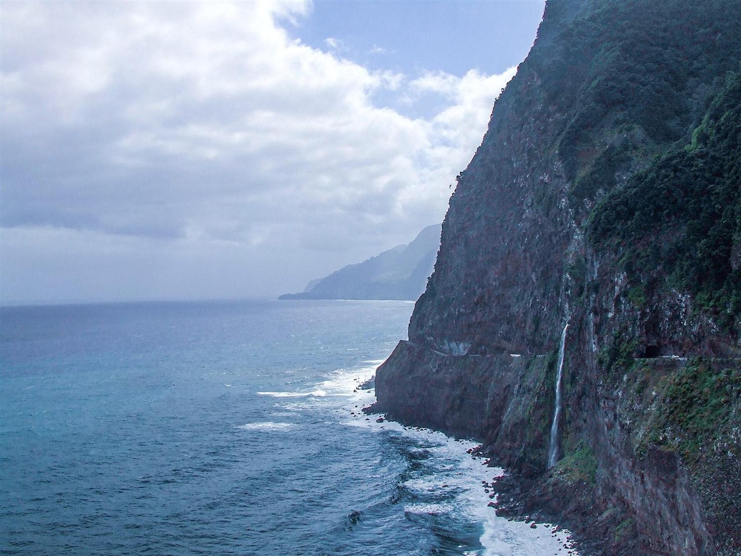 Steep cliffs and waterfall along the coast at Ribeira de Janela, Madeira, with a road cut into the rock