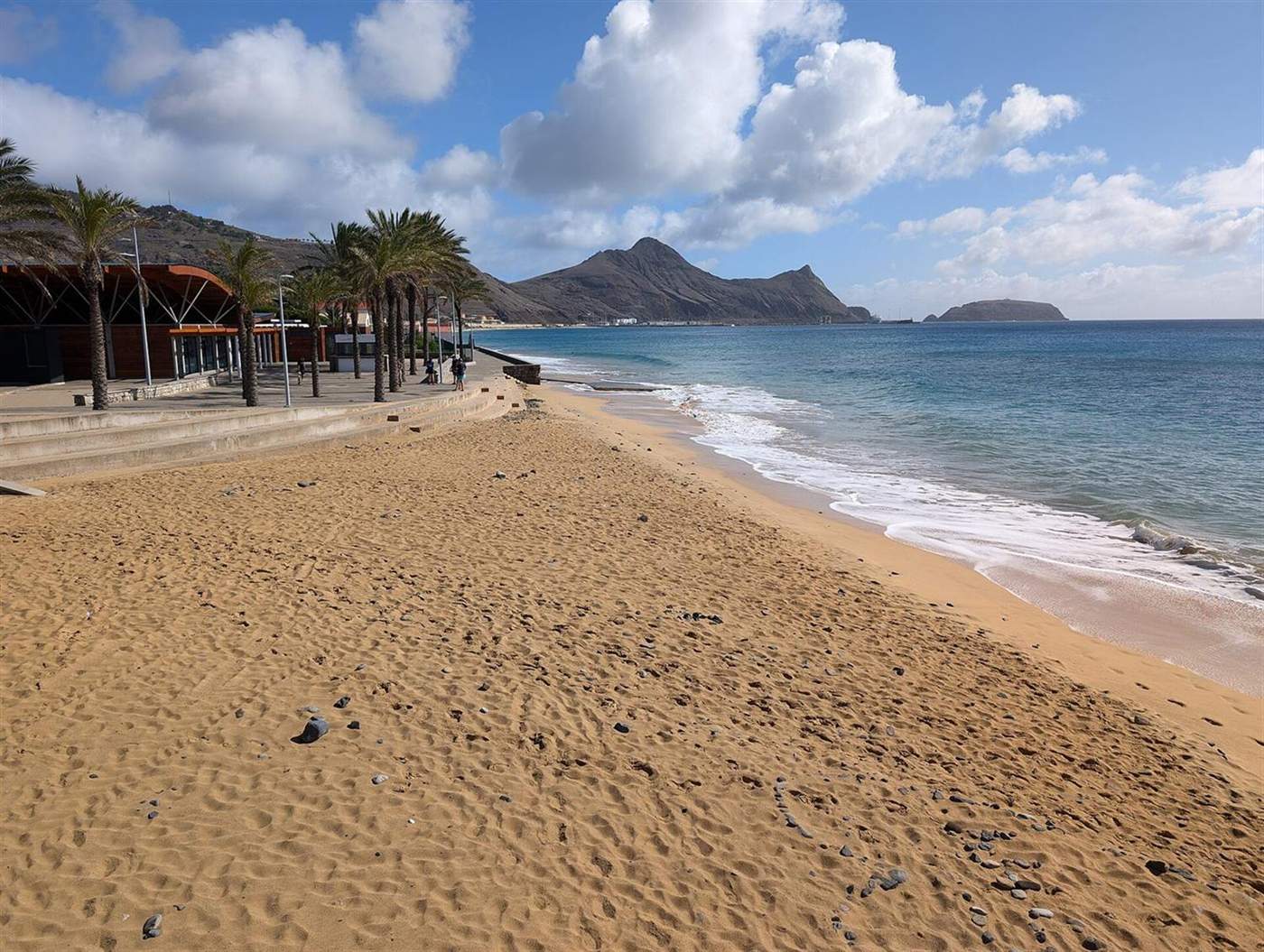 Gouden zandstrand met palmomzoomde promenade bij Cais Velho, Porto Santo, bergen aan de overkant van de baai
