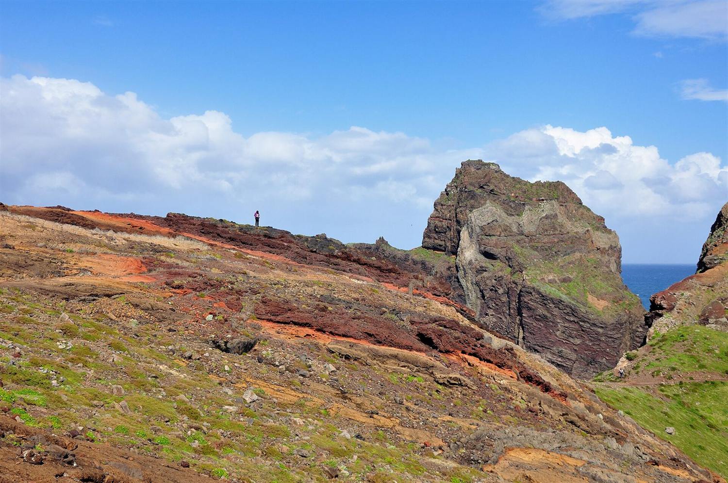 Rode en okerkleurige vulkanische bergkam bij Ponta de São Lourenço, Madeira, met een eenzame wandelaar en de zee op de achtergrond
