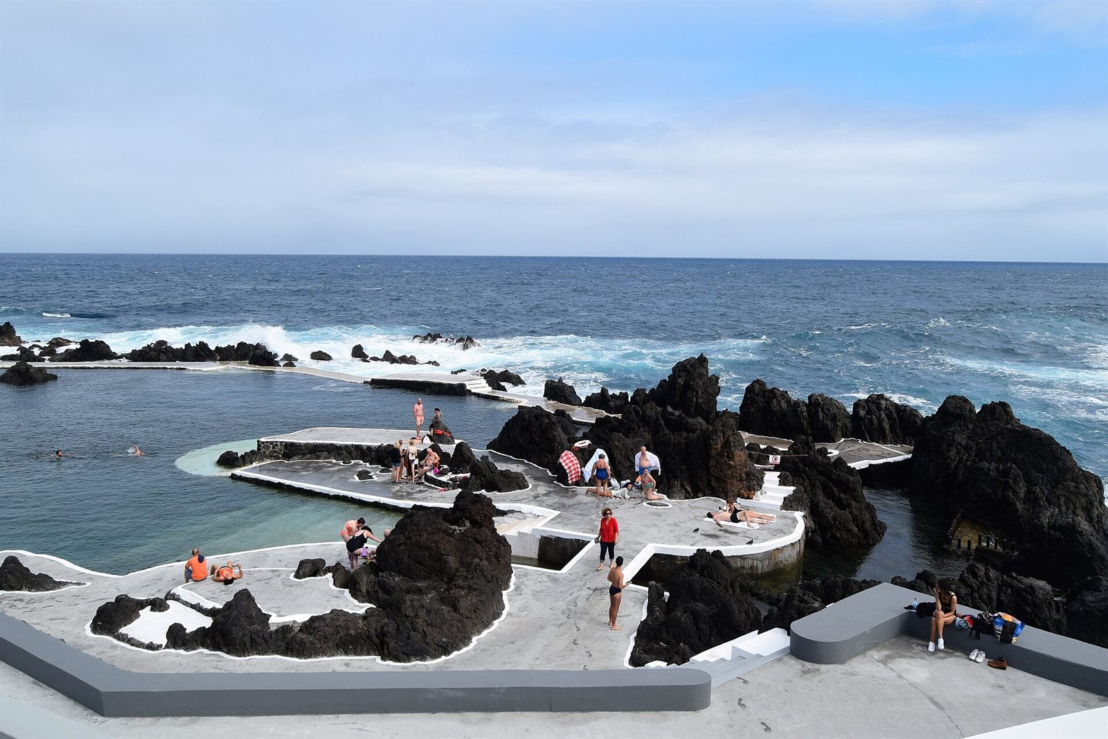 Natuurlijke vulkanische rotspoelen bij Porto Moniz, Madeira, met mensen die zonnebaden en zwemmen aan de zee