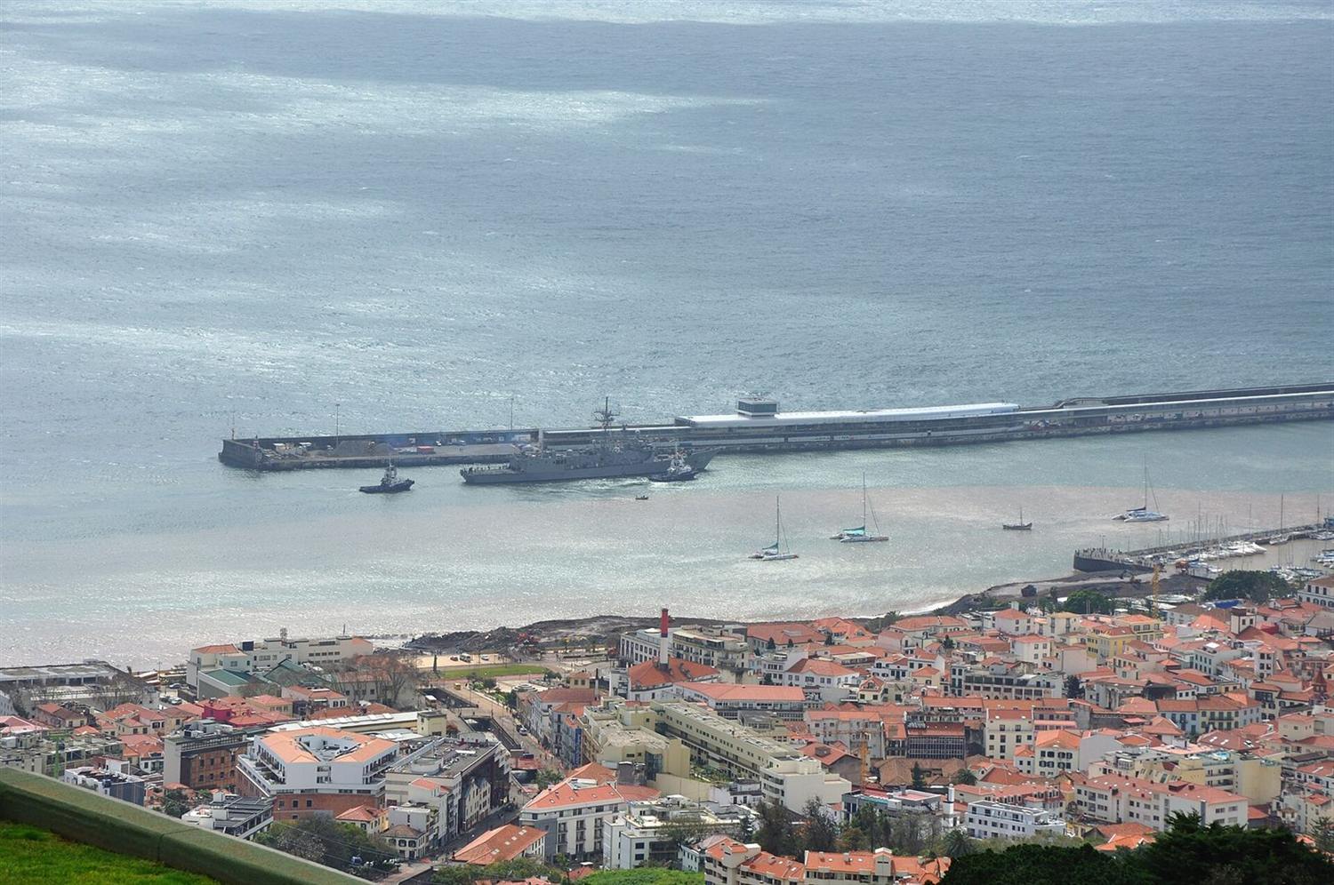 Luftaufnahme des Hafens von Funchal, Madeira, mit einem angedockten Marineschiff und der Stadt mit orangefarbenen Dächern darunter
